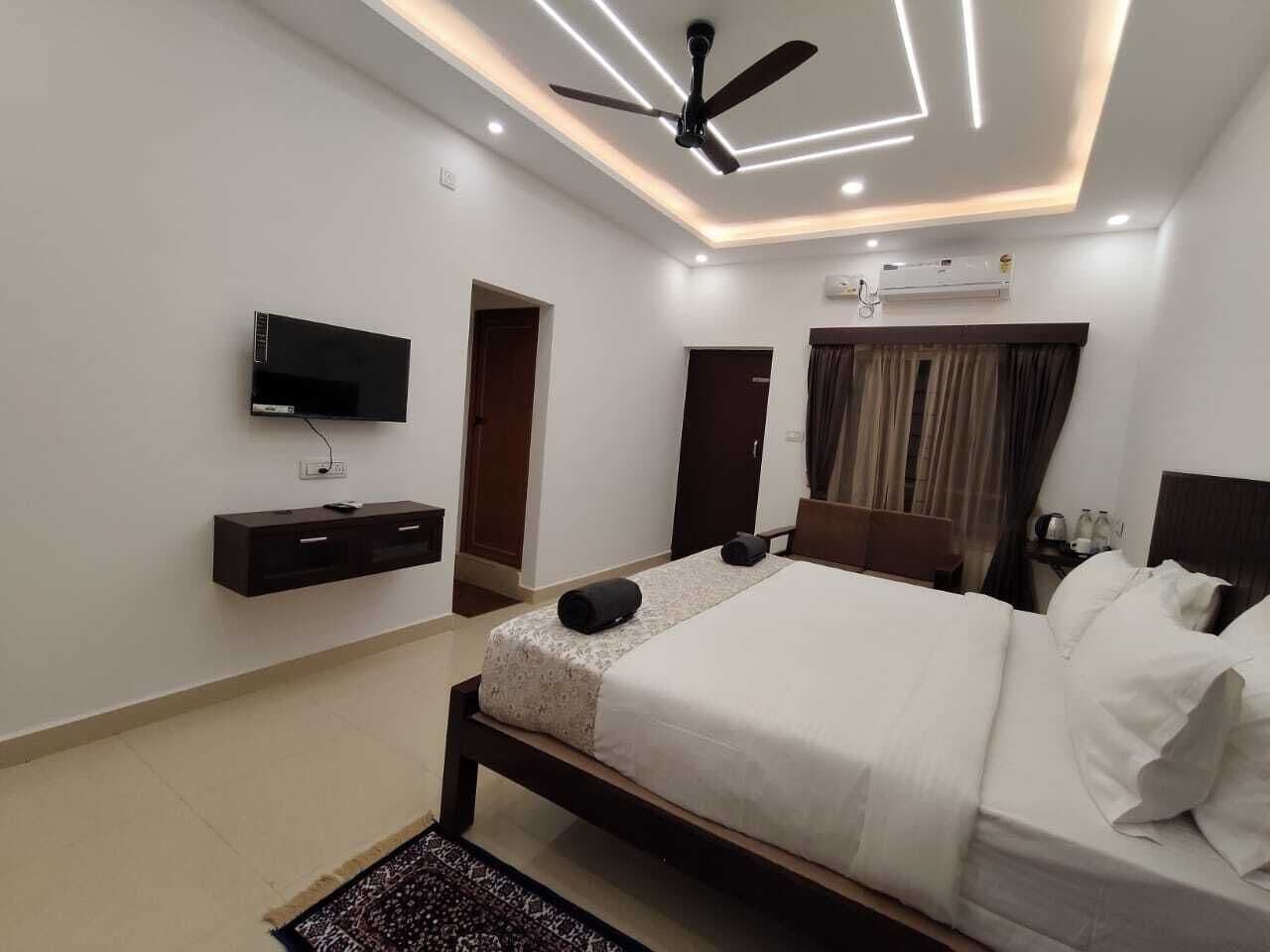 A modern hotel room with a bed, bedside tables, a TV, and a ceiling fan.