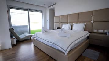 A modern hotel room with a large bed, a seating area with a chair, and a view through the window.