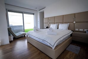 A modern hotel room with a large bed, a seating area with a chair, and a view through the window.