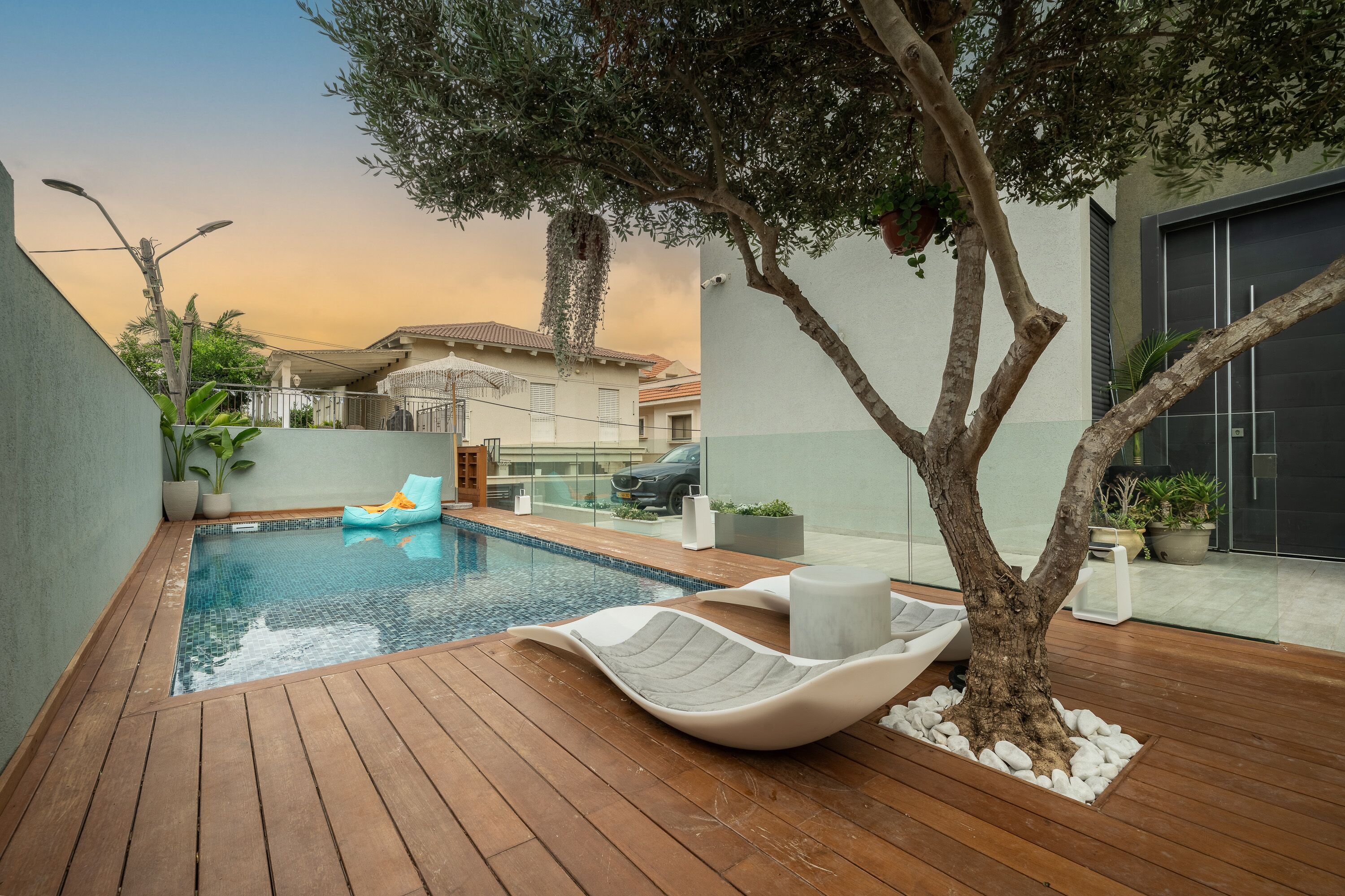 Una piscina con muelle de madera, sillas de descanso y un árbol.
