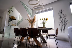 A modern dining area with a glass staircase, a dining table with chairs, and a vase of flowers.
