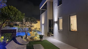 A modern outdoor patio with artificial grass, wicker furniture, and a pool.