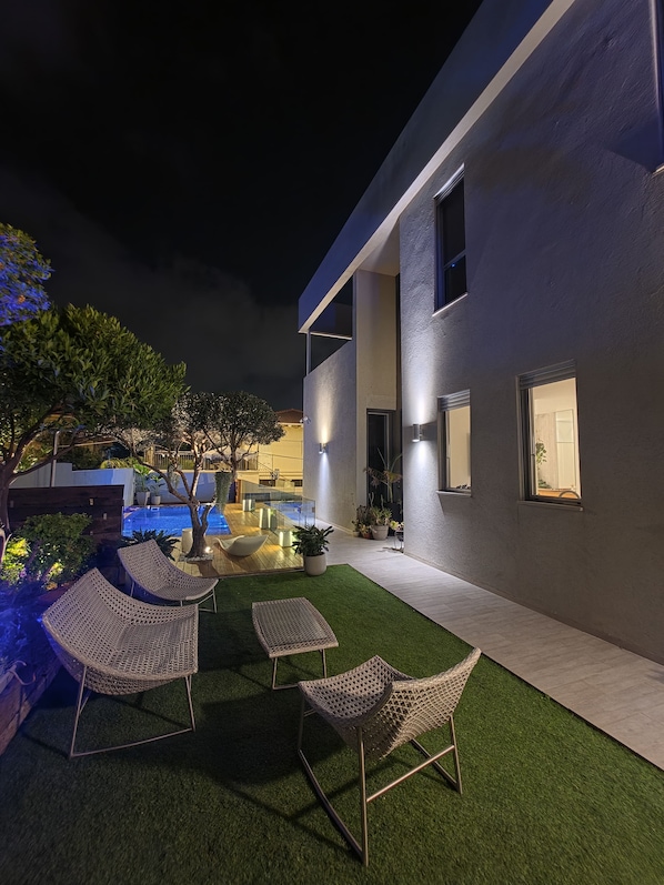 A modern outdoor patio with artificial grass, wicker furniture, and a pool.
