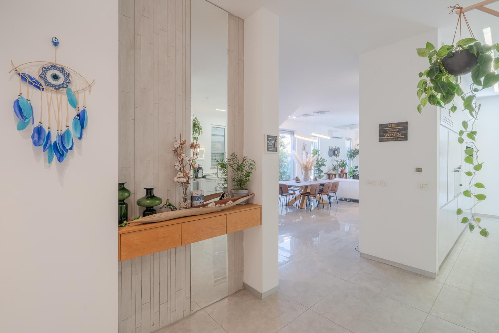 Un interior moderno con zona de comedor, un elemento decorativo en la pared y plantas en macetas.