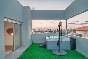 A balcony with a hot tub, artificial grass, and a view of a residential area.