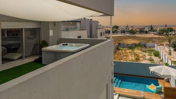 A modern outdoor pool area with a hot tub, a covered seating area, and a view of the surrounding neighborhood.