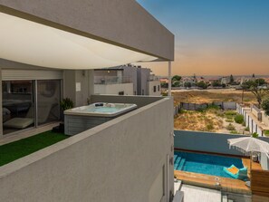 A modern outdoor pool area with a hot tub, a covered seating area, and a view of the surrounding neighborhood.