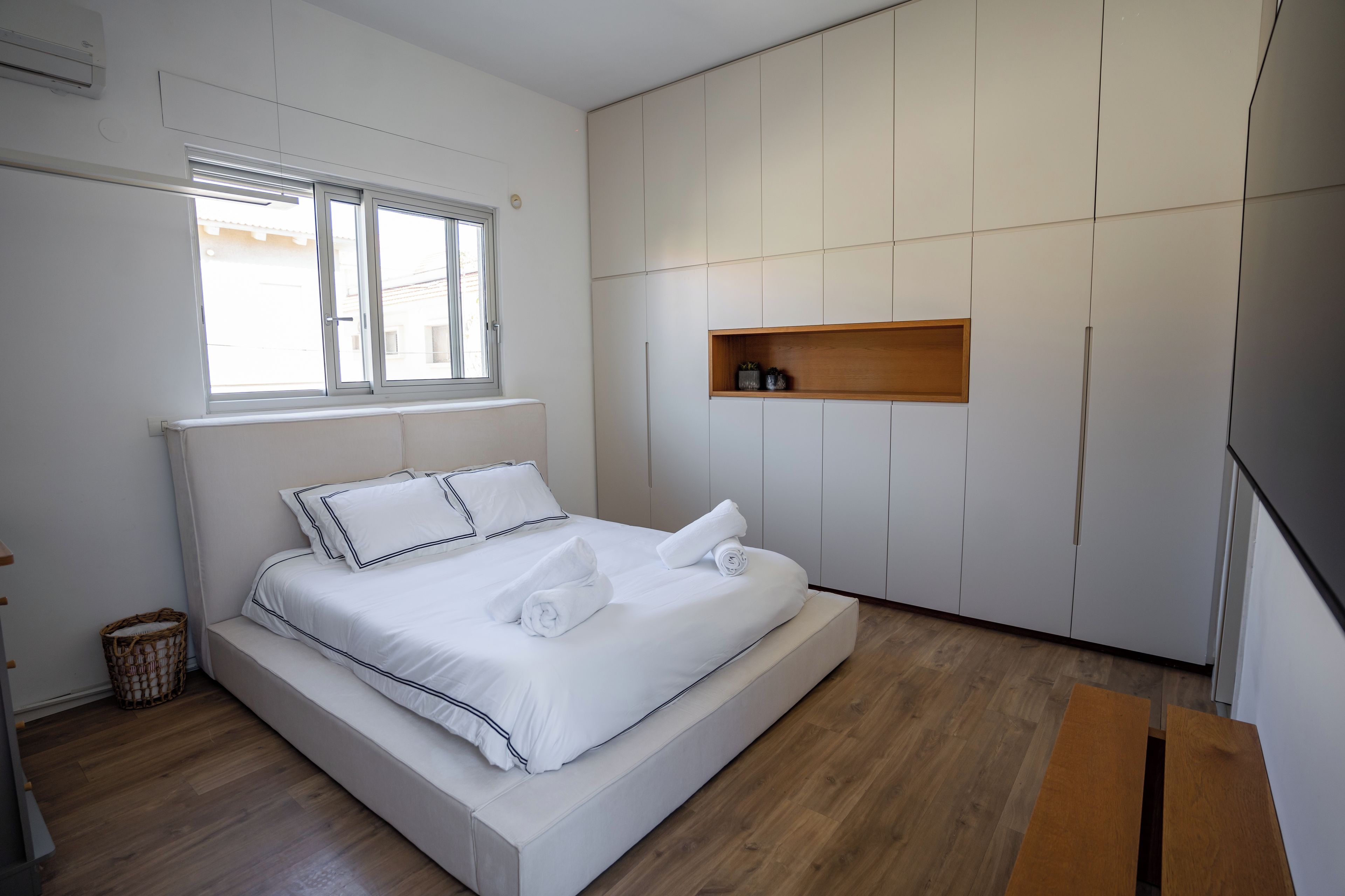 A modern bedroom with a large bed, a wooden shelf, and a window.
