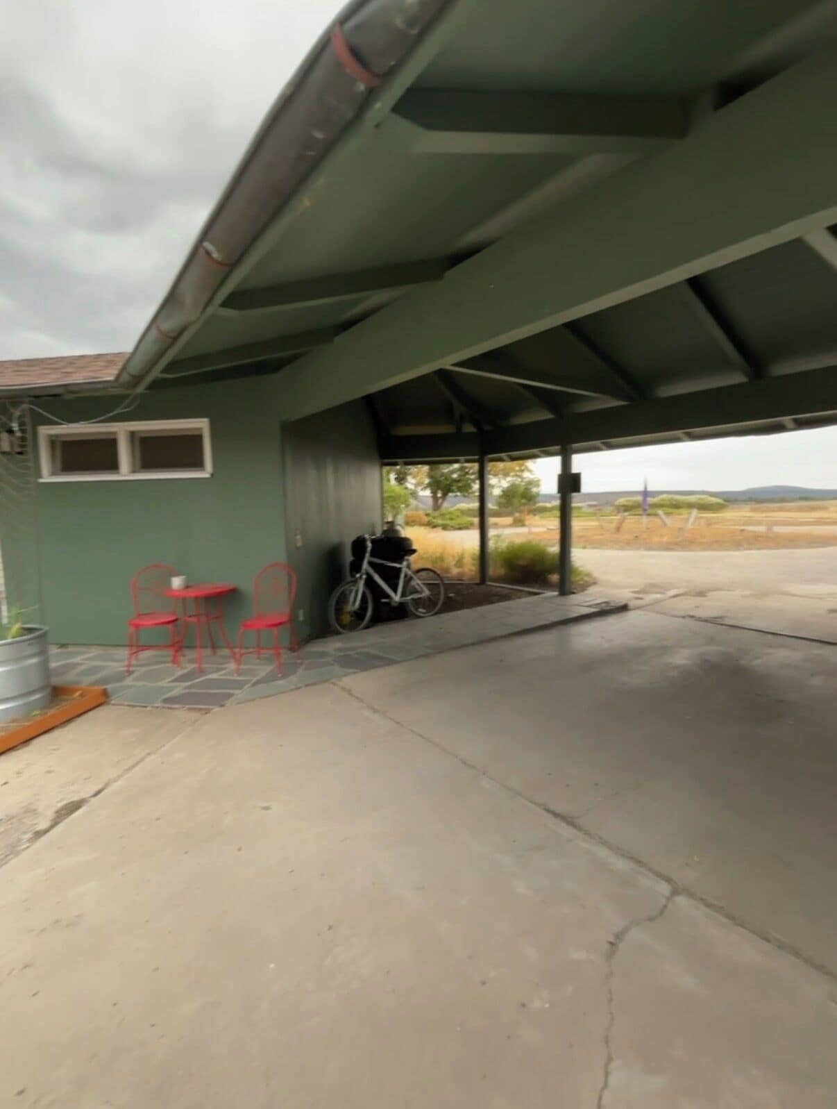 A covered outdoor area with a bicycle, red chairs, and a small table.