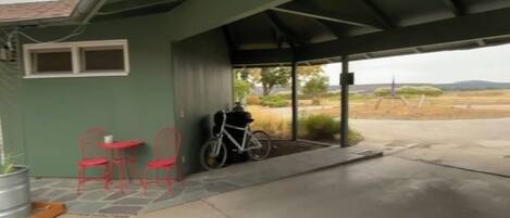 A covered outdoor area with a bicycle, red chairs, and a small table.