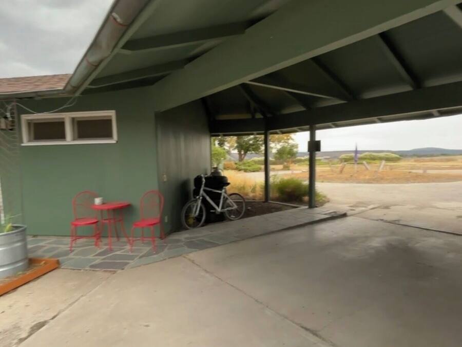 A covered outdoor area with a bicycle, red chairs, and a small table.