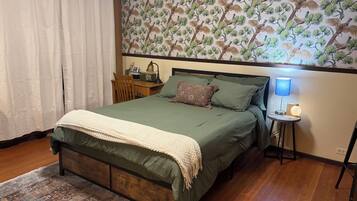 A bedroom with a bed, a nightstand, a lamp, and a wall with a bird pattern.