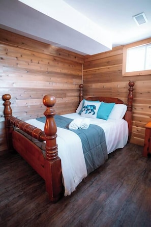 A wooden-paneled room with a bed, a window, and a wooden floor. - Beautiful River-front Log Cottage: Glass Room & Hot Tub (Kawartha Lakes)