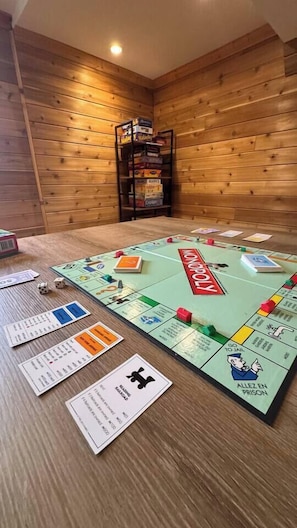 A Monopoly game set on a wooden floor with a bookshelf in the background. - Beautiful River-front Log Cottage: Glass Room & Hot Tub (Kawartha Lakes)