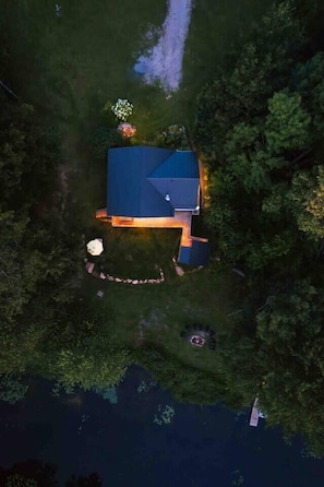 An aerial view of a house with a blue roof, surrounded by dense greenery and a body of water. - Beautiful River-front Log Cottage: Glass Room & Hot Tub (Kawartha Lakes)
