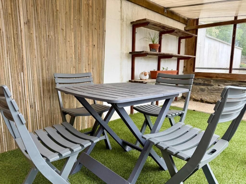 Une terrasse avec une table et des chaises, entourée d’une clôture en bois et donnant sur une fenêtre.