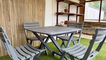 Une terrasse avec une table et des chaises, entourée d’une clôture en bois et donnant sur une fenêtre.