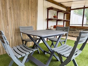 Une terrasse avec une table et des chaises, entourée d’une clôture en bois et donnant sur une fenêtre.
