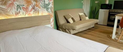 A room with a bed, a sofa, a small table, and a kitchenette area.