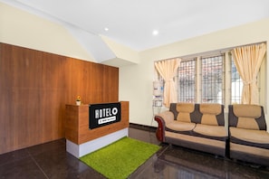 A hotel reception area with a wooden reception desk, a sofa, and a water dispenser. - Classic The Daffodils (Thiruvananthapuram)