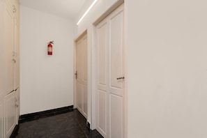 A corridor with white doors, a fire extinguisher mounted on the wall, and a black tiled floor. - Classic The Daffodils (Thiruvananthapuram)