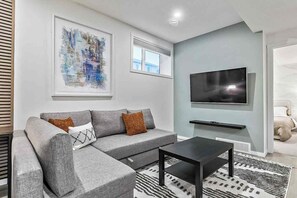 Un salon moderne avec un canapé d’angle gris, une table basse noire et un téléviseur fixé au mur.