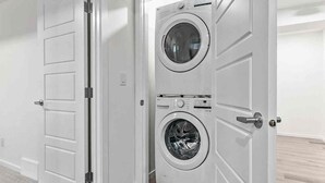 Una lavanderia con due lavatrici affiancate, una porta bianca e un pavimento in legno.