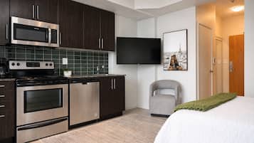 A modern kitchen with stainless steel appliances, a flat-screen TV, and a bed with a green blanket.