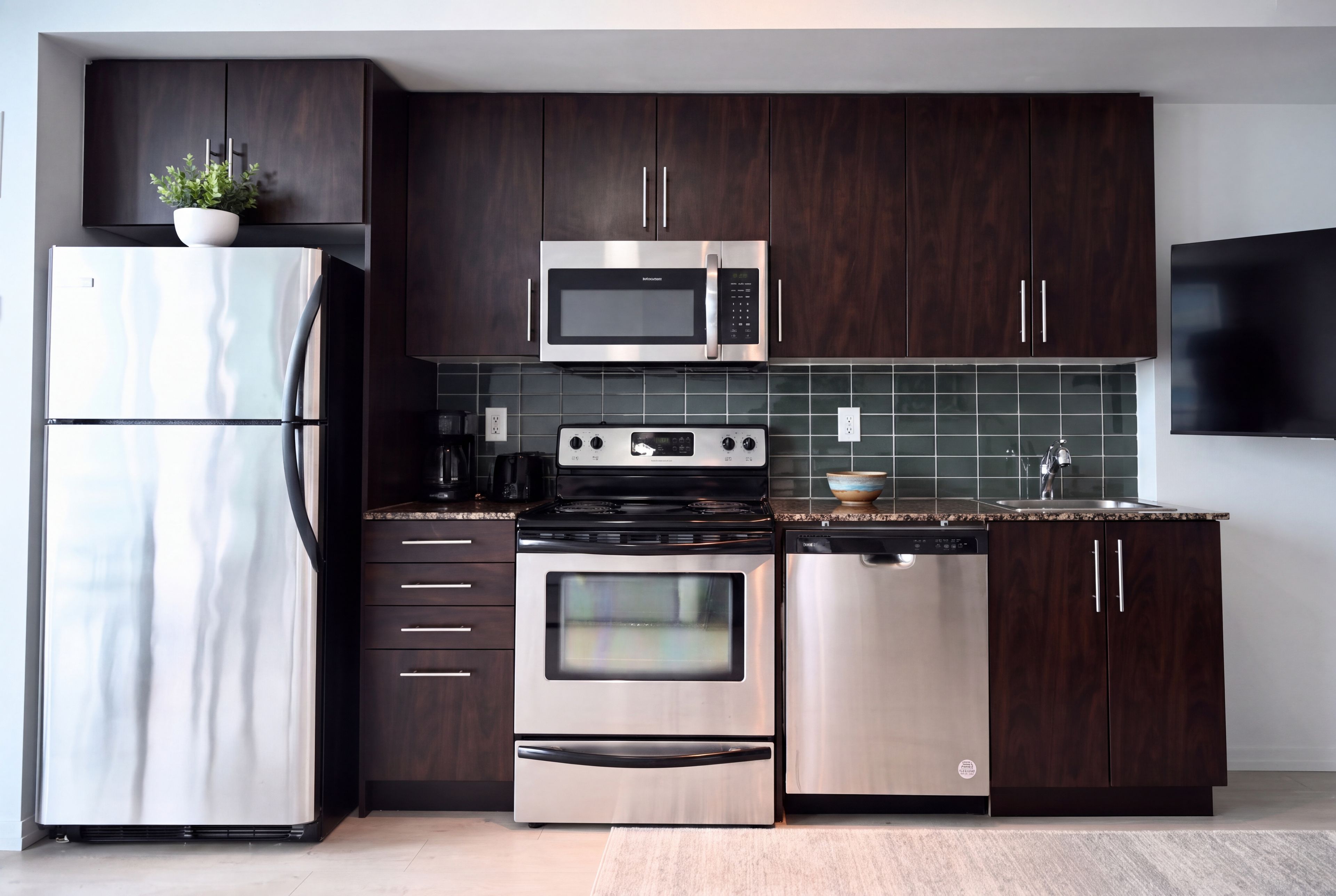 Une cuisine moderne avec des meubles de couleur bois foncé, des appareils électroménagers en acier inoxydable, un four à micro-ondes, un four et un lave-vaisselle.