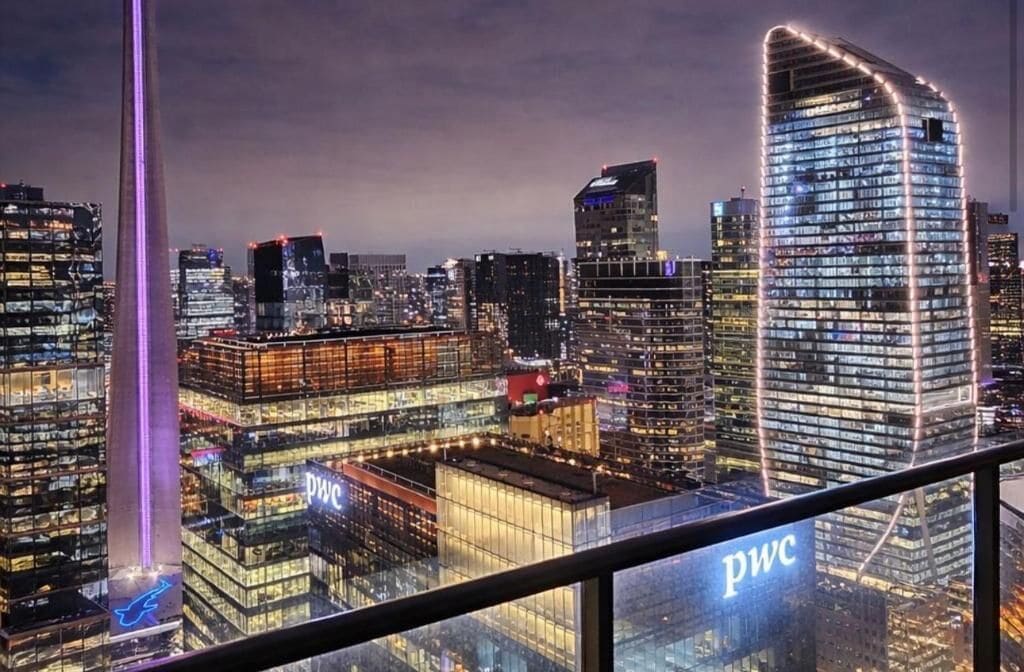 A cityscape with illuminated skyscrapers, including a prominent building with a curved facade and the 'PWC' logo.