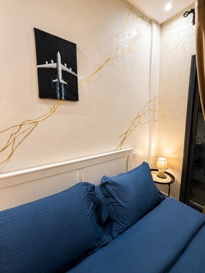Ein Schlafzimmer mit einem Bett, einem Nachttisch, einer Lampe und einem an der Wand hängenden Bild von einem Flugzeug.
