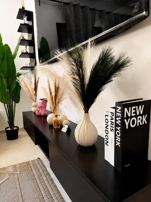 Ein modernes Wohnzimmer mit einem schwarzen Konsolentisch, Zimmerpflanzen und Büchern mit den Titeln 'New York' und 'Paris London'.