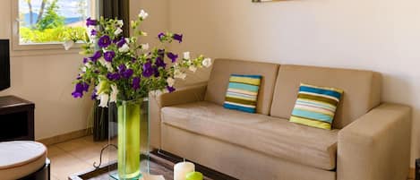 Una sala de estar con un sofá, una mesa de centro con libros y velas, un florero con flores y un cuadro en la pared.