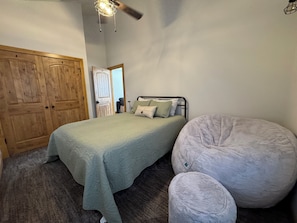 A bedroom with a bed, a large round chair, a wooden wardrobe, and a ceiling fan.