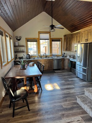 A kitchen with wooden cabinets, a dining table with chairs, a refrigerator, and a ceiling fan.