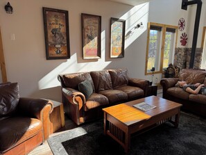 A cozy living room with leather sofas, a wooden coffee table, and framed vintage posters on the wall.