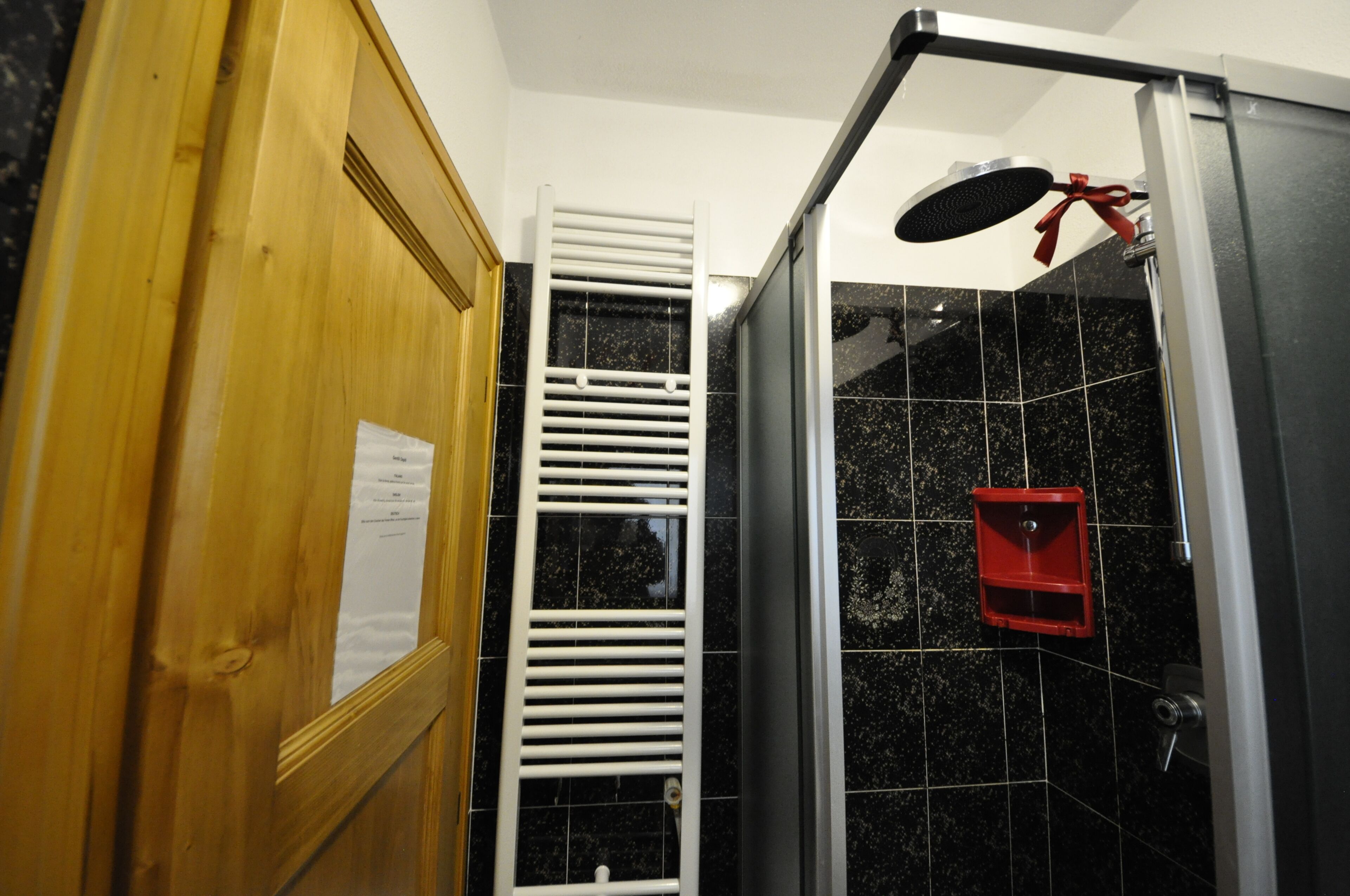 Une salle de bain avec une porte en bois, un porte-serviettes blanc, un mur recouvert de carreaux noirs et un objet rouge accroché au mur.