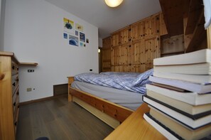 Un dormitorio con una cama de madera, un armario de madera y un escritorio pequeño con una pila de libros.