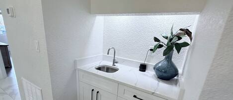 A small kitchen with white cabinetry, a sink, and a vase with a plant.