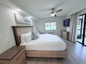Un dormitorio con una cama grande, ventilador de techo, ventana con vistas y una mesita de noche.