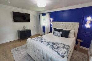 A bedroom with a large bed, a flat-screen TV, a bedside table, and a nightstand. - Stylish 4BR Boutique Home with Movie Lounge (Marietta)
