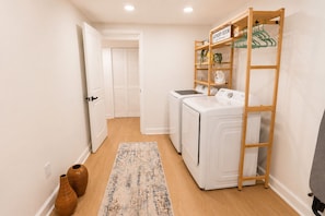 A laundry room with a wooden shelf, two washing machines, and a drying rack. - Stylish 4BR Boutique Home with Movie Lounge (Marietta)