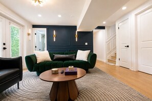 A modern living room with a green sofa, a round wooden coffee table, and a staircase in the background. - Stylish 4BR Boutique Home with Movie Lounge (Marietta)
