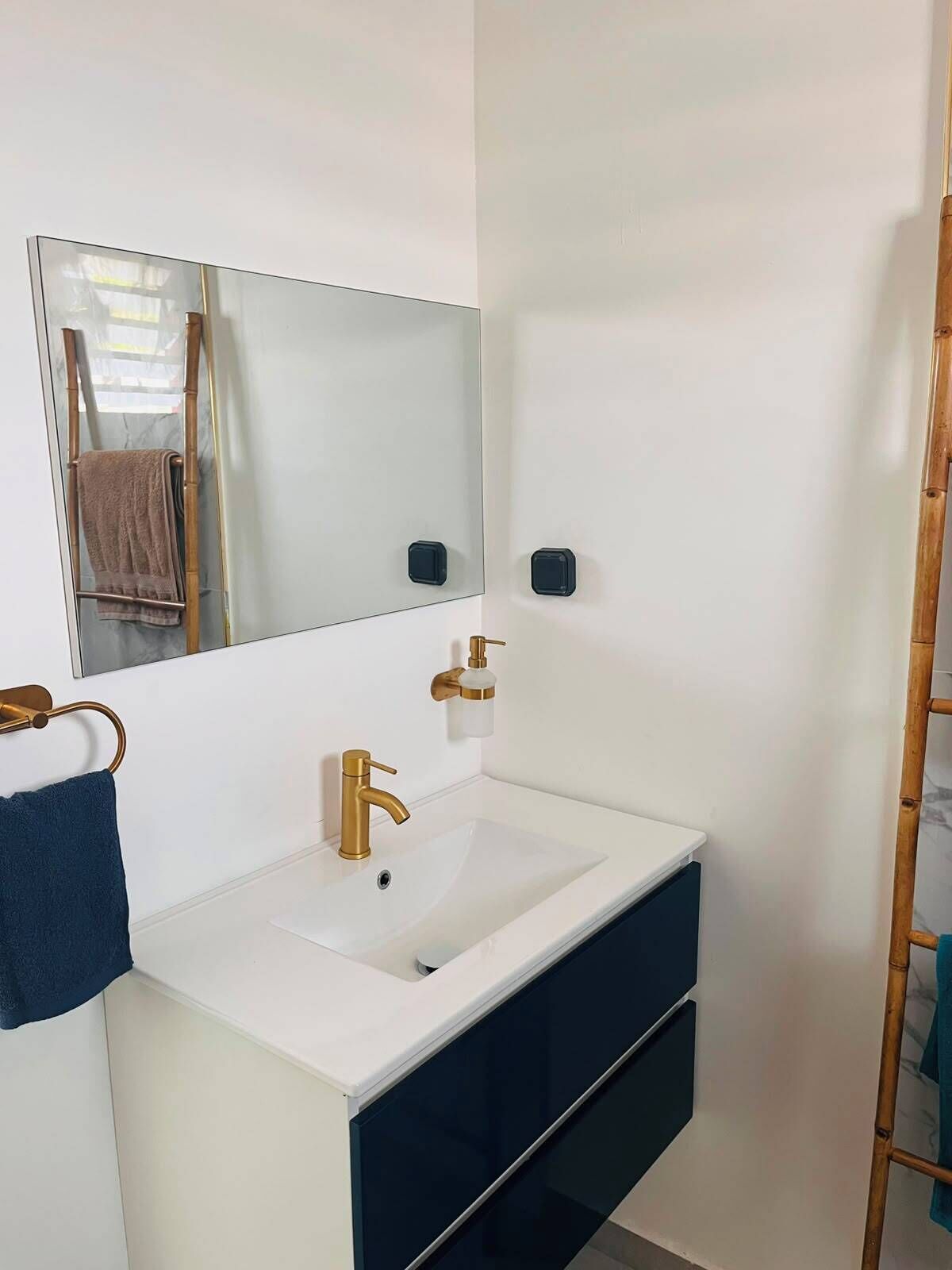 A bathroom with a white sink, gold faucet, and a mirror above it. There is a towel rack with a blue towel and a brown towel.