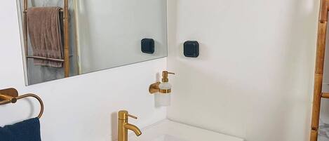 A bathroom with a white sink, gold faucet, and a mirror above it. There is a towel rack with a blue towel and a brown towel.