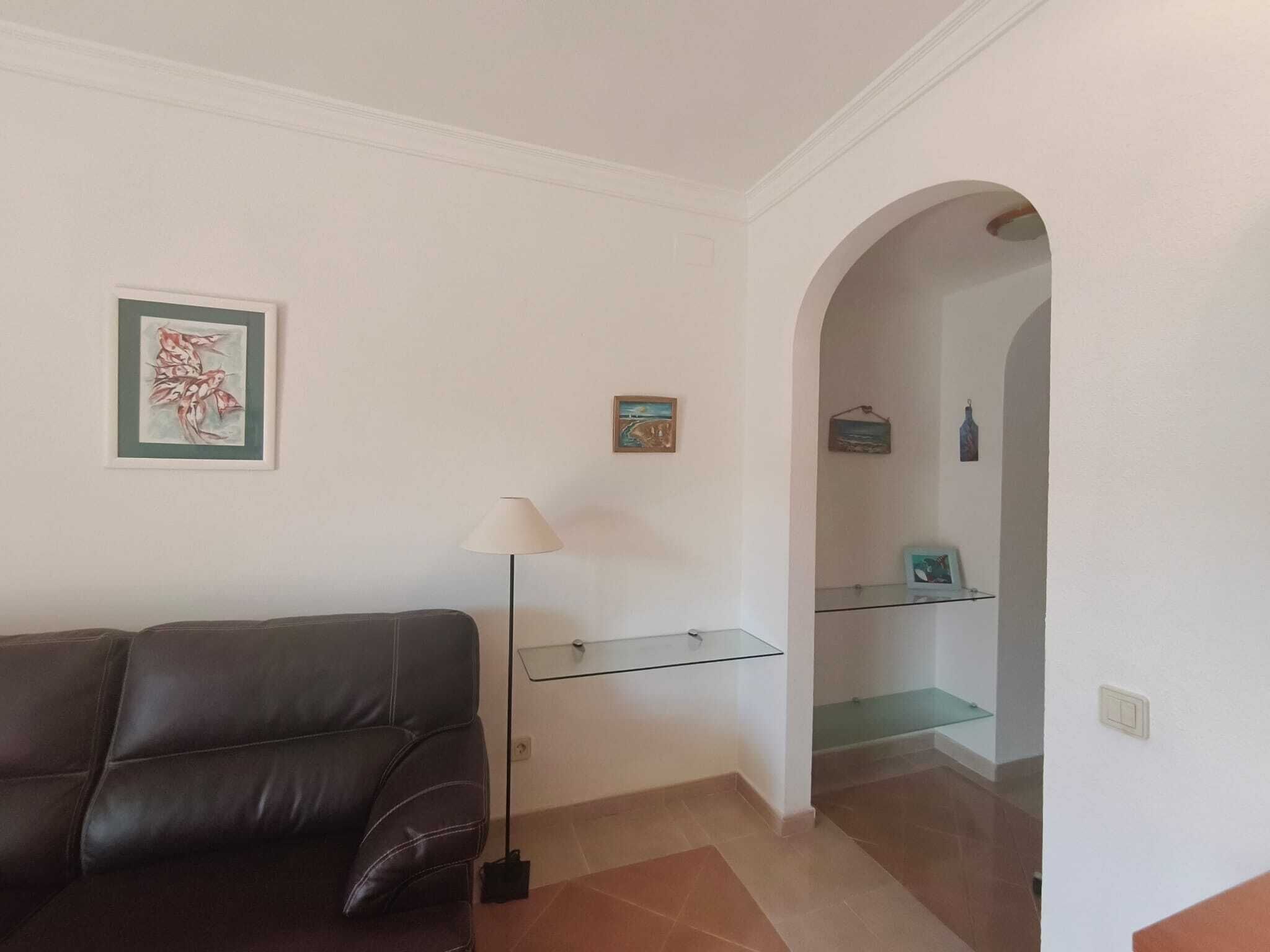 Ein Wohnzimmer mit einem dunkelbraunen Ledersofa, einer Stehlampe und einem Glastischchen mit Kunstwerken.