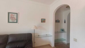 Ein Wohnzimmer mit einem dunkelbraunen Ledersofa, einer Stehlampe und einem Glastischchen mit Kunstwerken.