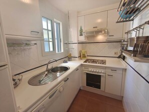 A compact kitchen with a sink, stove, and dishwasher, featuring white cabinetry and a window. - Family Apartment in Punta del Moral (Isla Canela) (Ayamonte)
