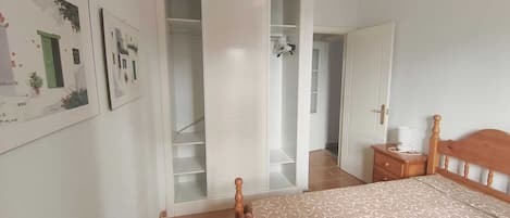 A bedroom with a bed, a wooden headboard, a nightstand, a wardrobe, and a door leading to another room.