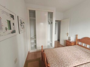 Ein Schlafzimmer mit einem Bett, einem Holzkopfende, einem Nachttisch, einem Kleiderschrank und einer Tür zu einem anderen Raum.